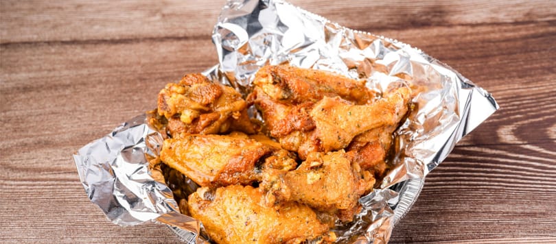 Golden-brown chicken wings in a foil container on a wooden surface.